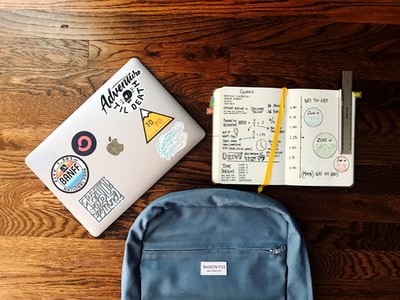书旁蓝色背包和银色MacBook平板摄影